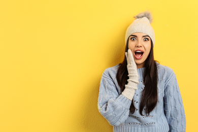 Photo of Emotional young woman in warm clothes on yellow background, space for text. Winter vacation