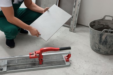 Photo of Worker holding tile near cutter on floor, closeup