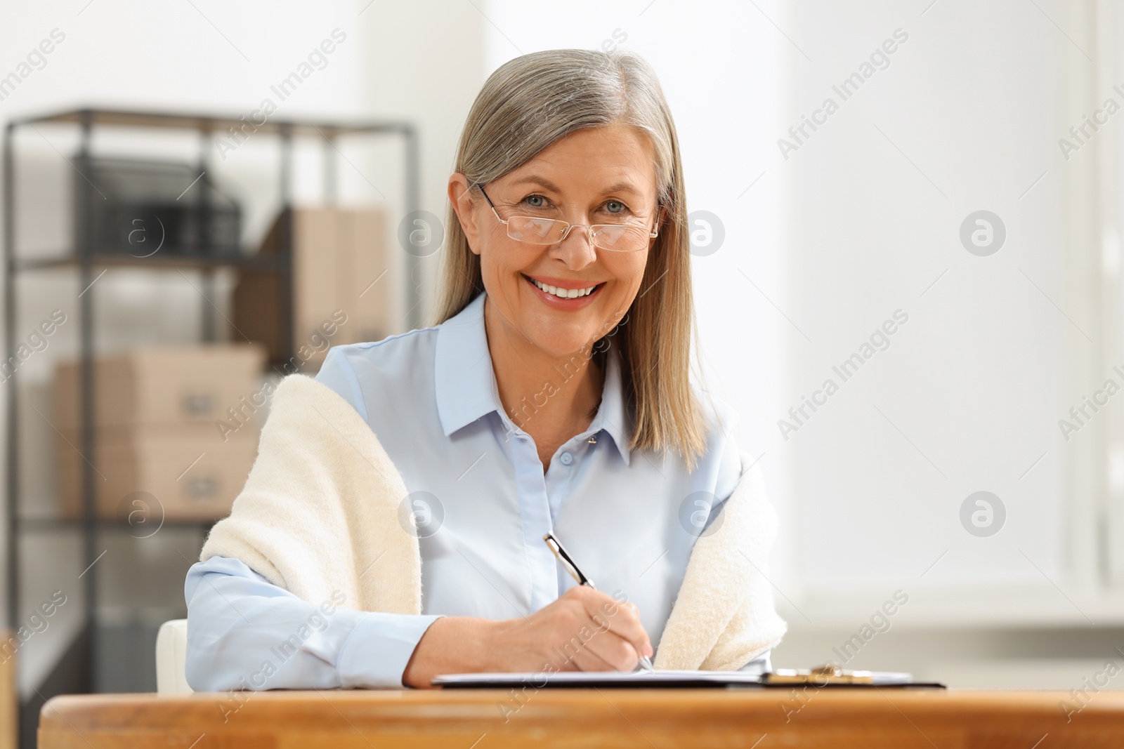 Photo of Smiling senior woman signing Last Will and Testament at table indoors