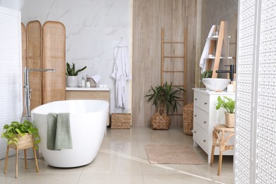 Modern white tub and beautiful green houseplants in bathroom. Interior design