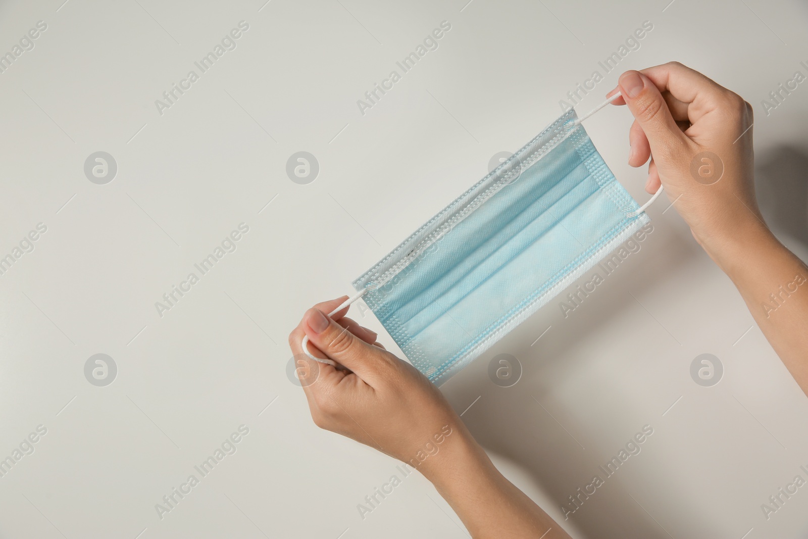 Photo of Woman holding disposable face mask on light background, closeup with space for text. Protective measures during coronavirus quarantine