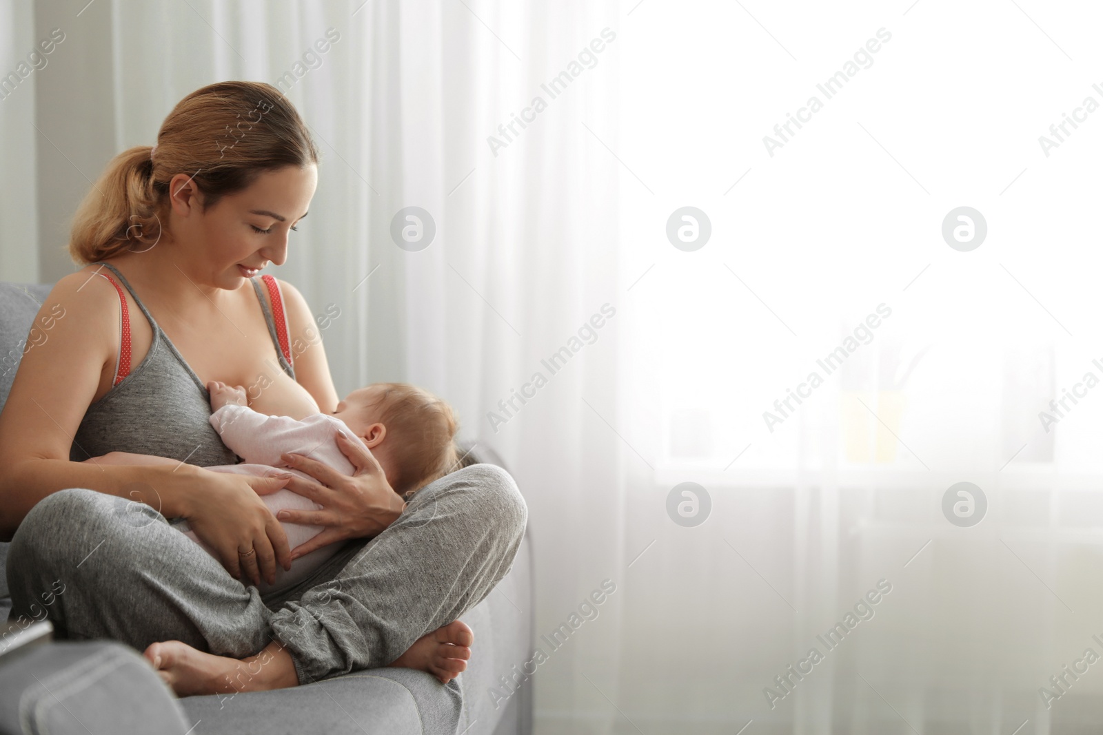 Photo of Young woman breastfeeding her baby at home. Space for text