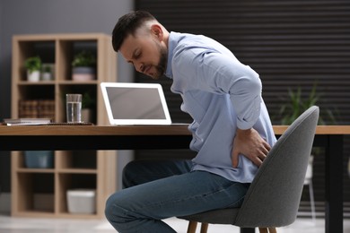 Photo of Man suffering from back pain while working with laptop in office. Symptom of poor posture