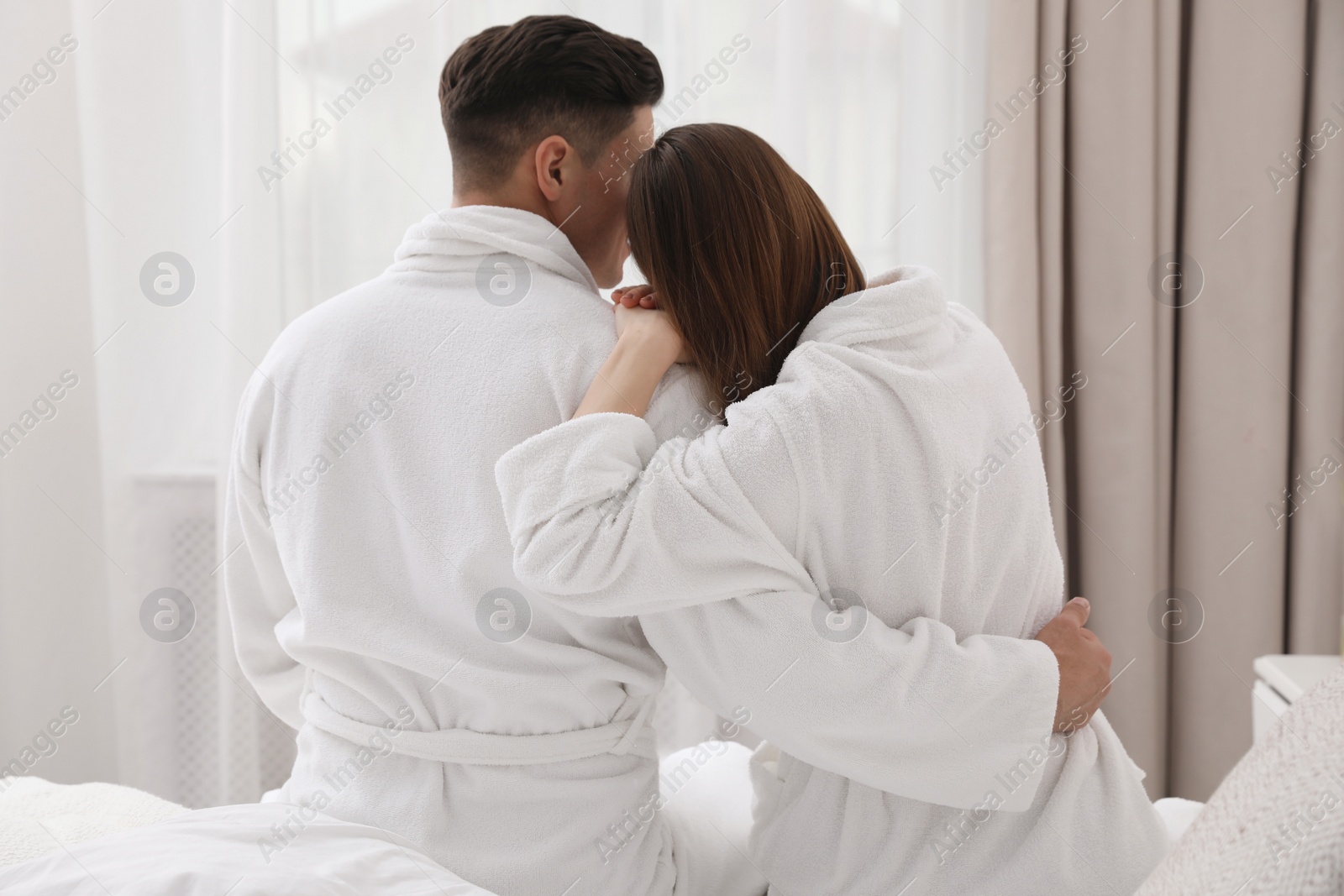 Photo of Happy couple in bathrobes sitting on bed at home