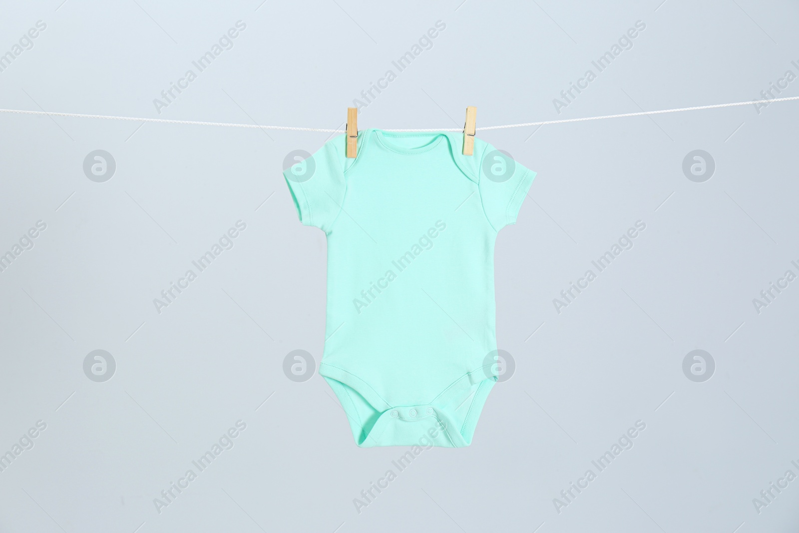 Photo of Cute baby onesie hanging on clothes line against light grey background. Laundry day