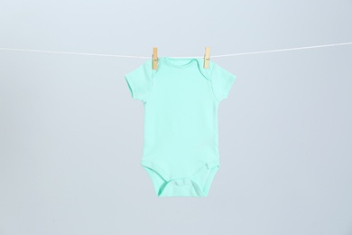 Cute baby onesie hanging on clothes line against light grey background. Laundry day