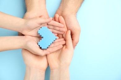 Top view of parents and kid holding blue heart in hands on turquoise background, space for text. Family day