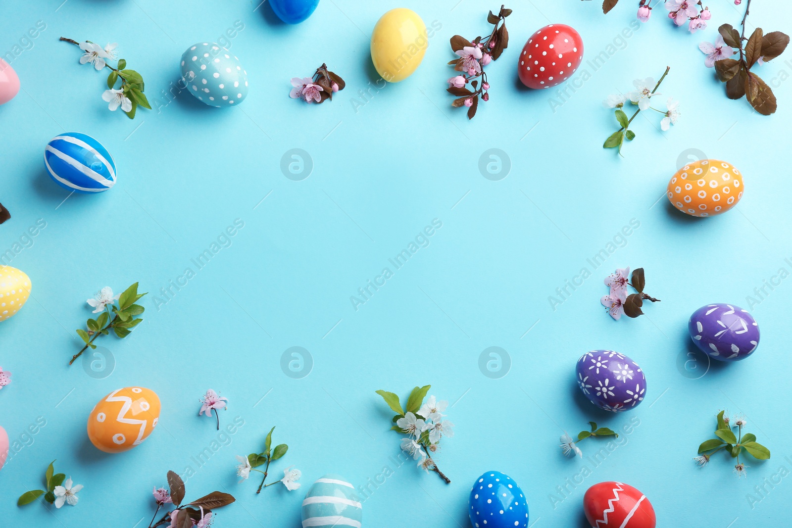 Photo of Frame made of painted Easter eggs and blossoming branches on color background, top view. Space for text