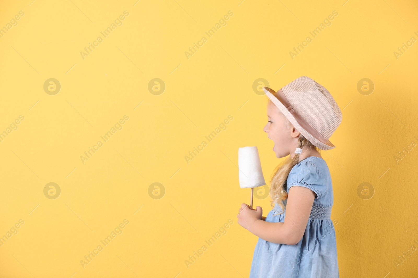 Photo of Cute little girl with cotton candy on color background. Space for text