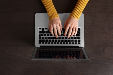 Woman working with laptop at wooden table, top view