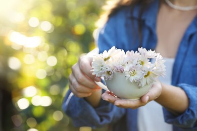 Photo of Woman holding cup with beautiful white chamomile flowers outdoors, closeup. Space for text