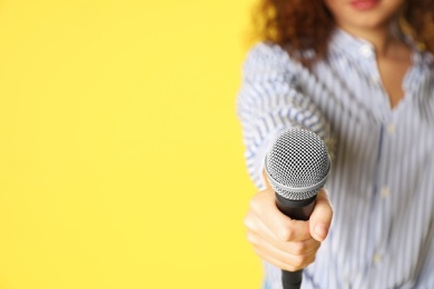 Young woman holding microphone on color background, closeup with space for text