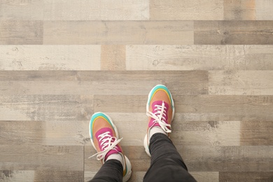Photo of Woman in colorful sneakers standing on wooden floor, top view. Space for text