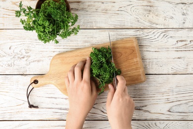 Photo of Woman cutting fresh green parsley at white wooden table, top view