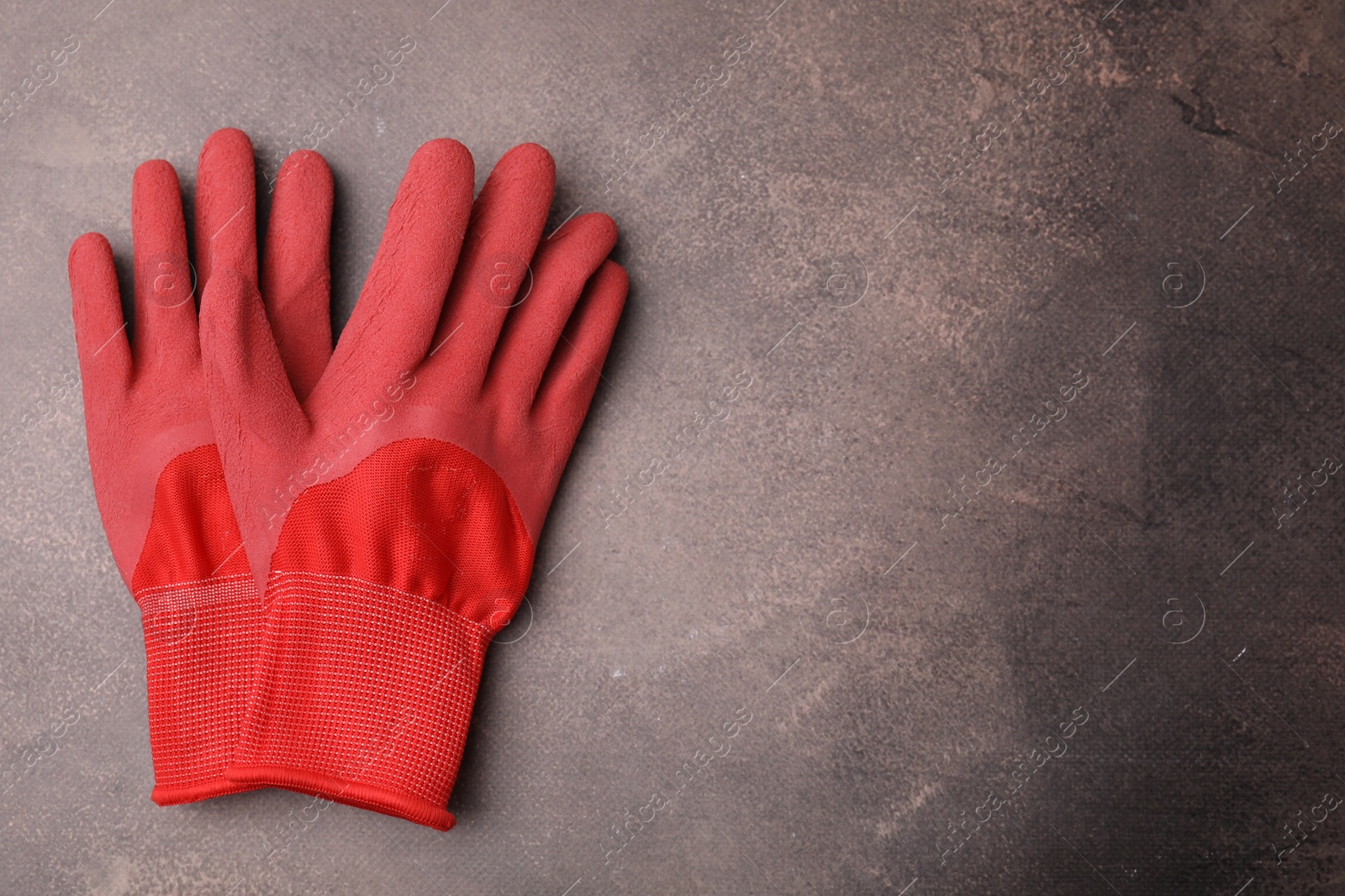 Photo of Pair of red gardening gloves on brown textured table, top view. Space for text