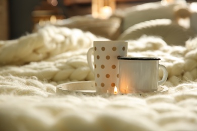 Photo of Tray with cups on cozy knitted blanket in room. Interior design