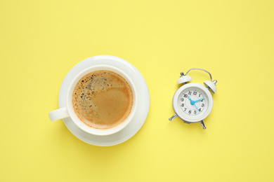 Photo of Cup of morning coffee and alarm clock on yellow background, flat lay