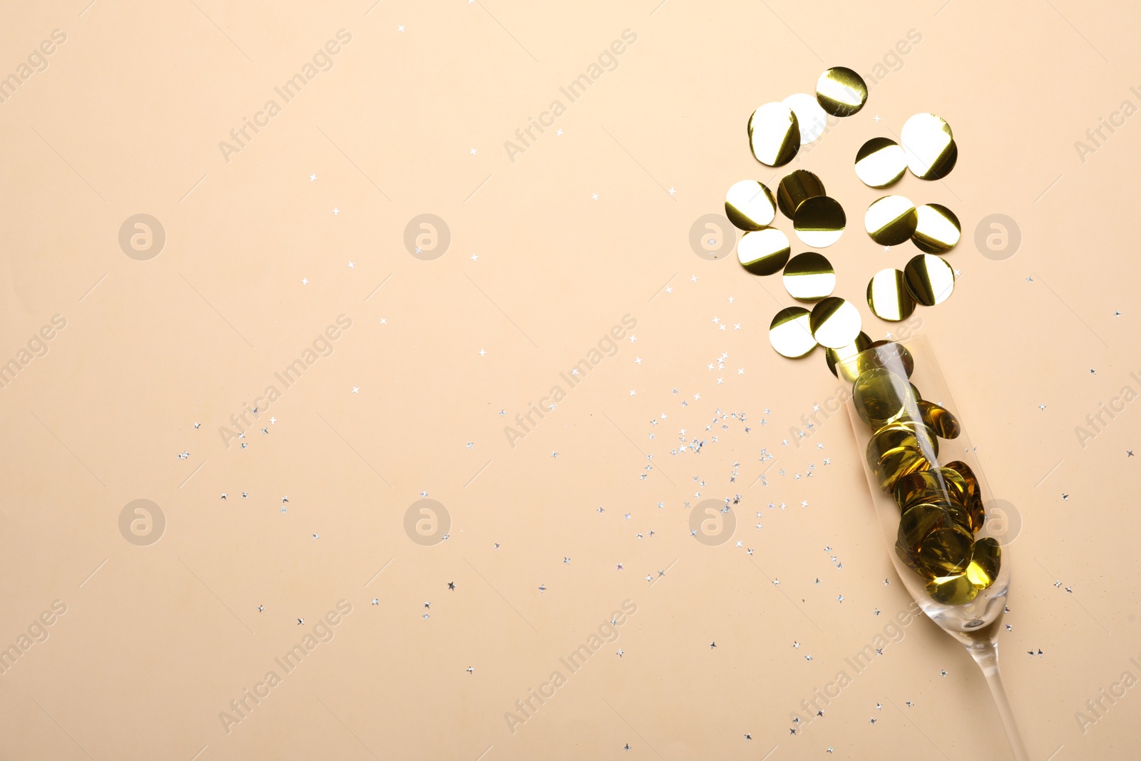 Photo of Glass with shiny confetti on beige background, flat lay. Space for text