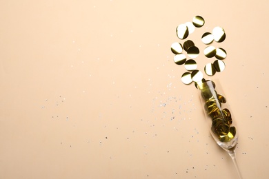 Glass with shiny confetti on beige background, flat lay. Space for text