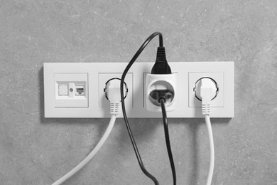 Many different electrical power plugs in sockets on grey wall
