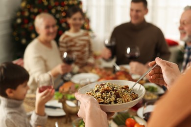 Photo of Woman with bowl of traditional Christmas kutia and her family at festive dinner, focus on hands. Slavic dish