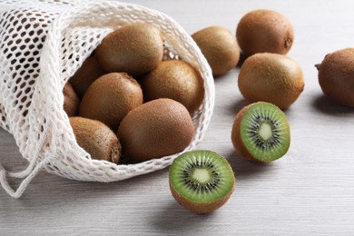 Photo of Net bag with cut and whole fresh kiwis on white wooden table