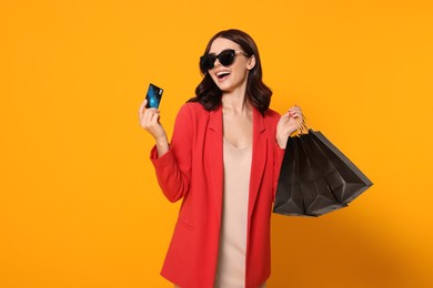 Photo of Beautiful young woman with paper shopping bags and credit card on yellow background