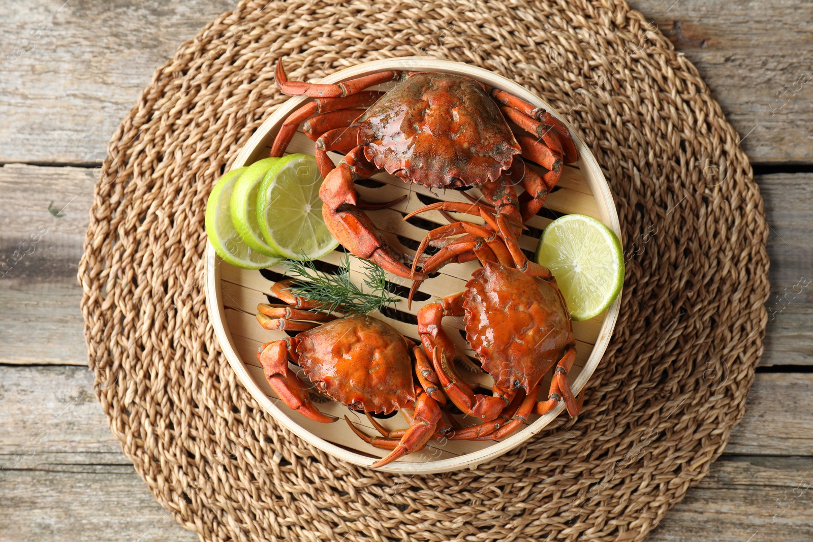 Photo of Delicious boiled crabs with lime and dill in bamboo steamer on wooden table, top view