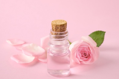 Photo of Bottle of essential oil and rose on pink background
