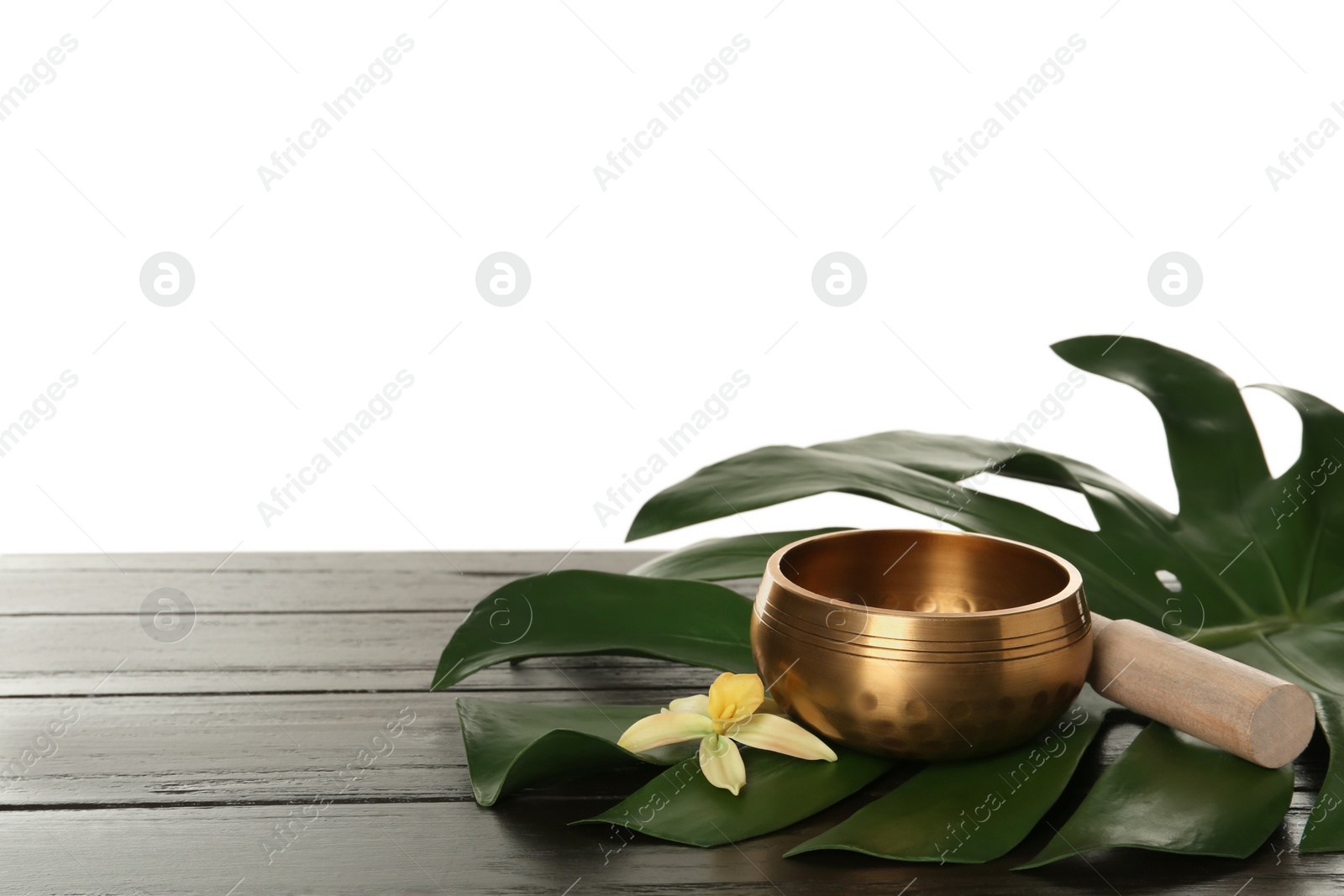 Photo of Golden singing bowl, mallet, green leaf and flower on wooden table against white background, space for text