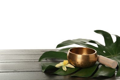 Photo of Golden singing bowl, mallet, green leaf and flower on wooden table against white background, space for text