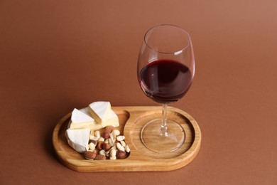 Photo of Glass of red wine, cheese and nuts on brown background