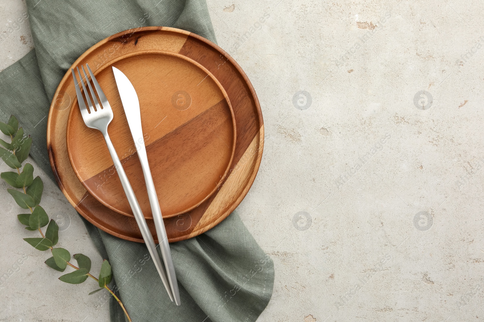 Photo of Stylish setting with cutlery, napkin, eucalyptus branch and plates on light table, top view. Space for text