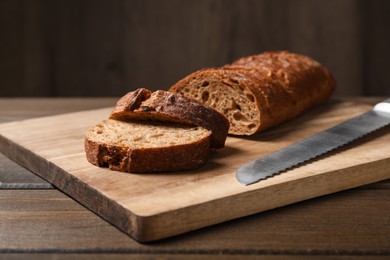 Cut rye baguette with knife on wooden table