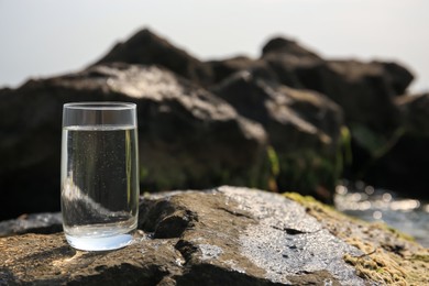 Glass of fresh water on stone outdoors, space for text