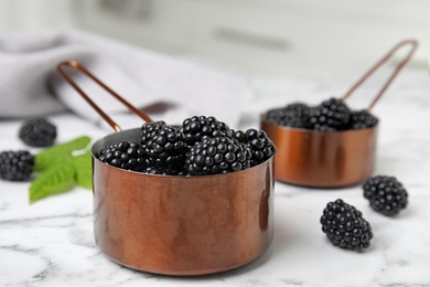 Photo of Metal saucepans with ripe blackberries on marble table