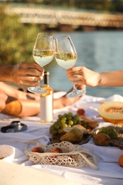 Photo of Couple clinking glasses with wine on pier at picnic, closeup