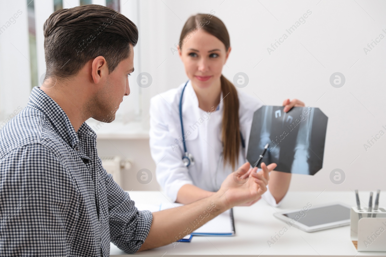 Photo of Orthopedist showing X-ray picture to patient at table in clinic