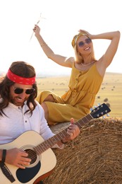 Photo of Beautiful hippie woman listening to her friend playing guitar in field