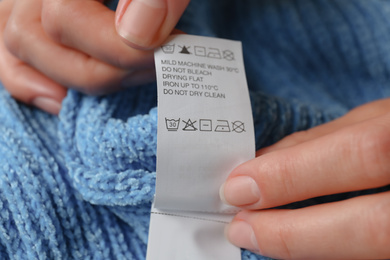 Woman reading clothing label with care symbols on blue knitted sweater, closeup