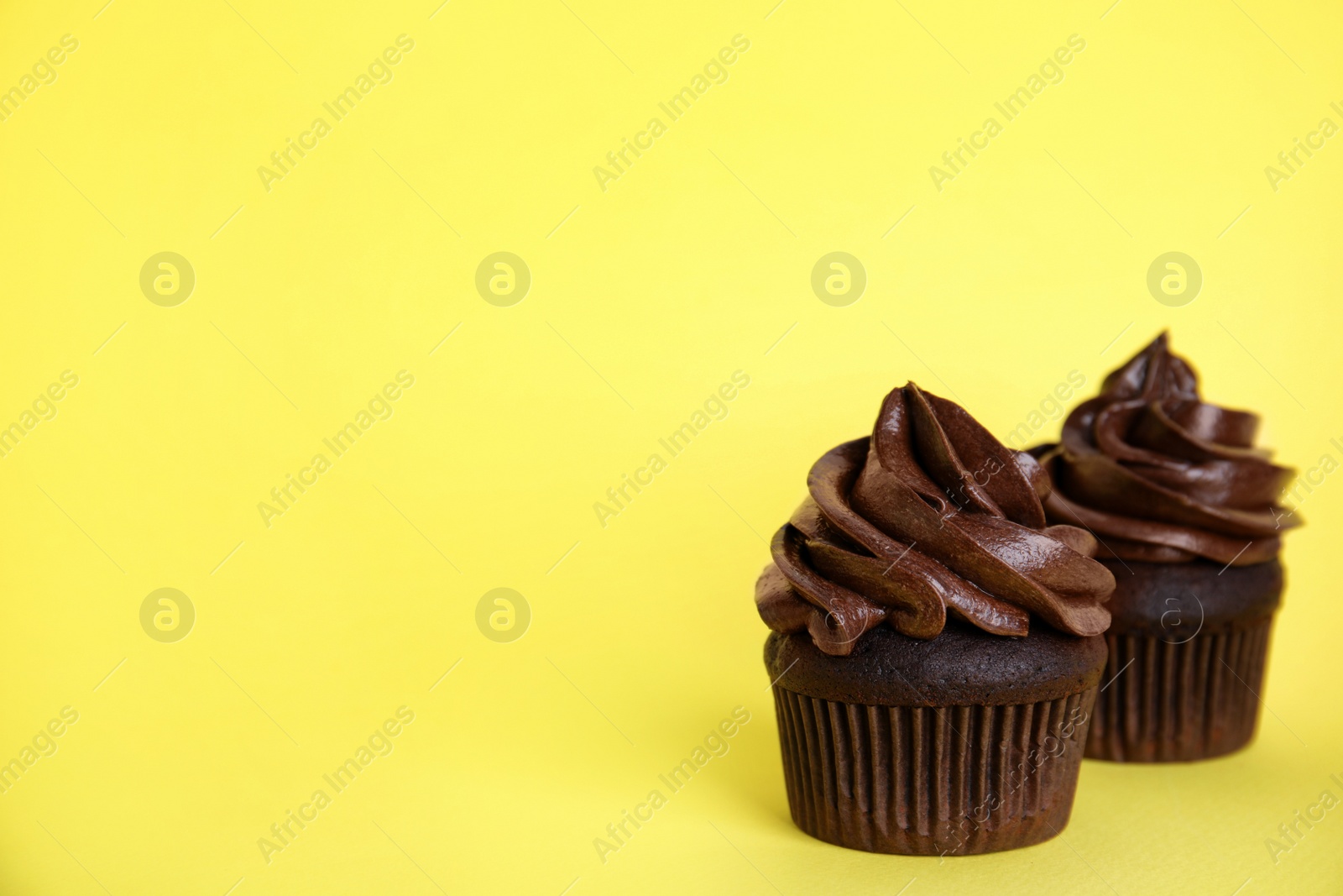 Photo of Delicious chocolate cupcakes with cream on yellow background. Space for text