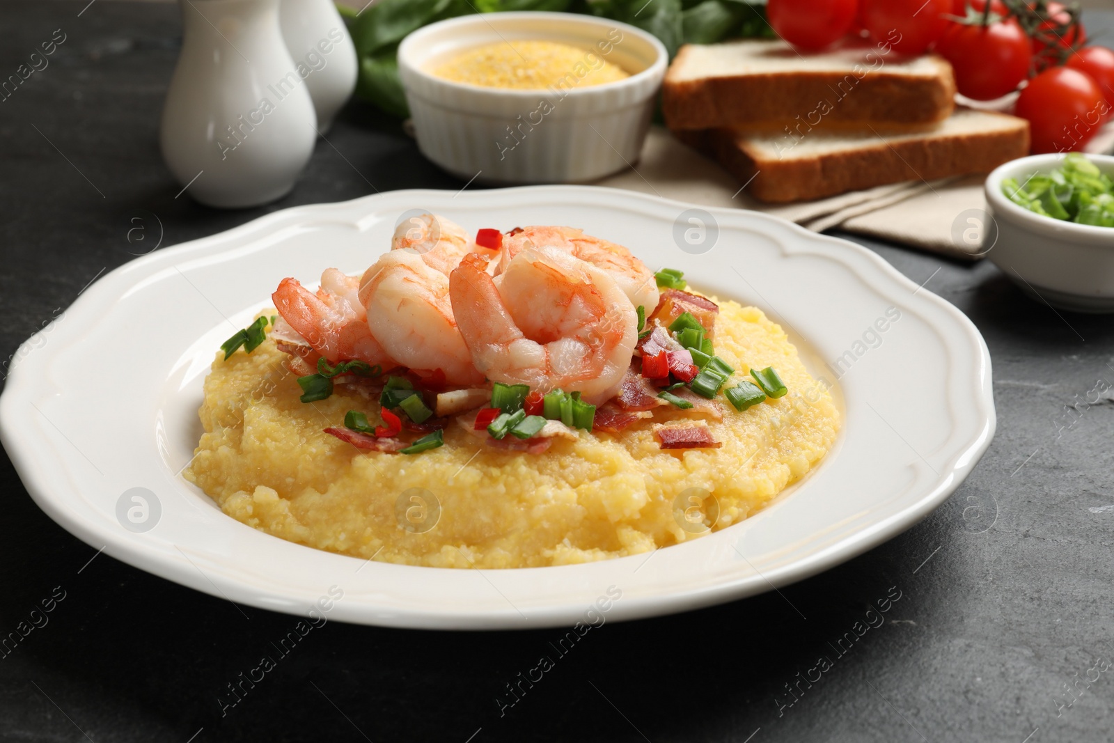 Photo of Plate with fresh tasty shrimps, bacon, grits, green onion and pepper on black table, closeup