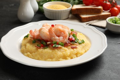 Photo of Plate with fresh tasty shrimps, bacon, grits, green onion and pepper on black table, closeup