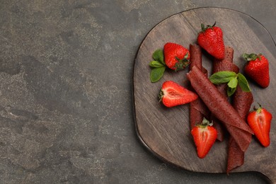 Photo of Delicious fruit leather rolls and strawberries on grey table, top view. Space for text