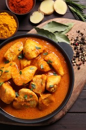 Delicious chicken curry in pan on wooden table, flat lay