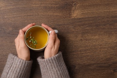 Photo of Woman holding cup of tasty herbal tea with thyme at wooden table, top view. Space for text