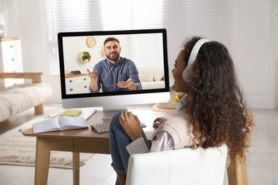 African American woman with headphones and modern computer at online lesson in room. E-learning