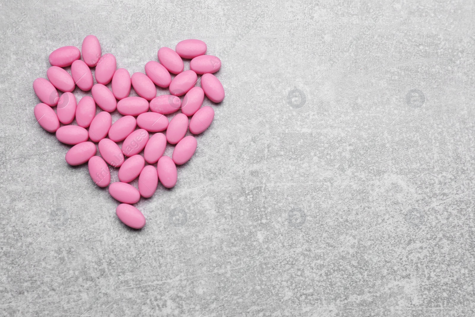 Photo of Heart made of pink dragee candies on grey textured background, flat lay. Space for text