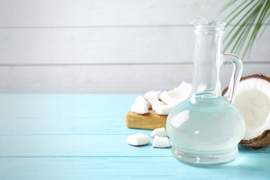 Photo of Coconut and jug with oil on light blue wooden table, space for text