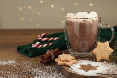 Photo of Hot drink with marshmallows, cookies and cinnamon on wooden table. Space for text